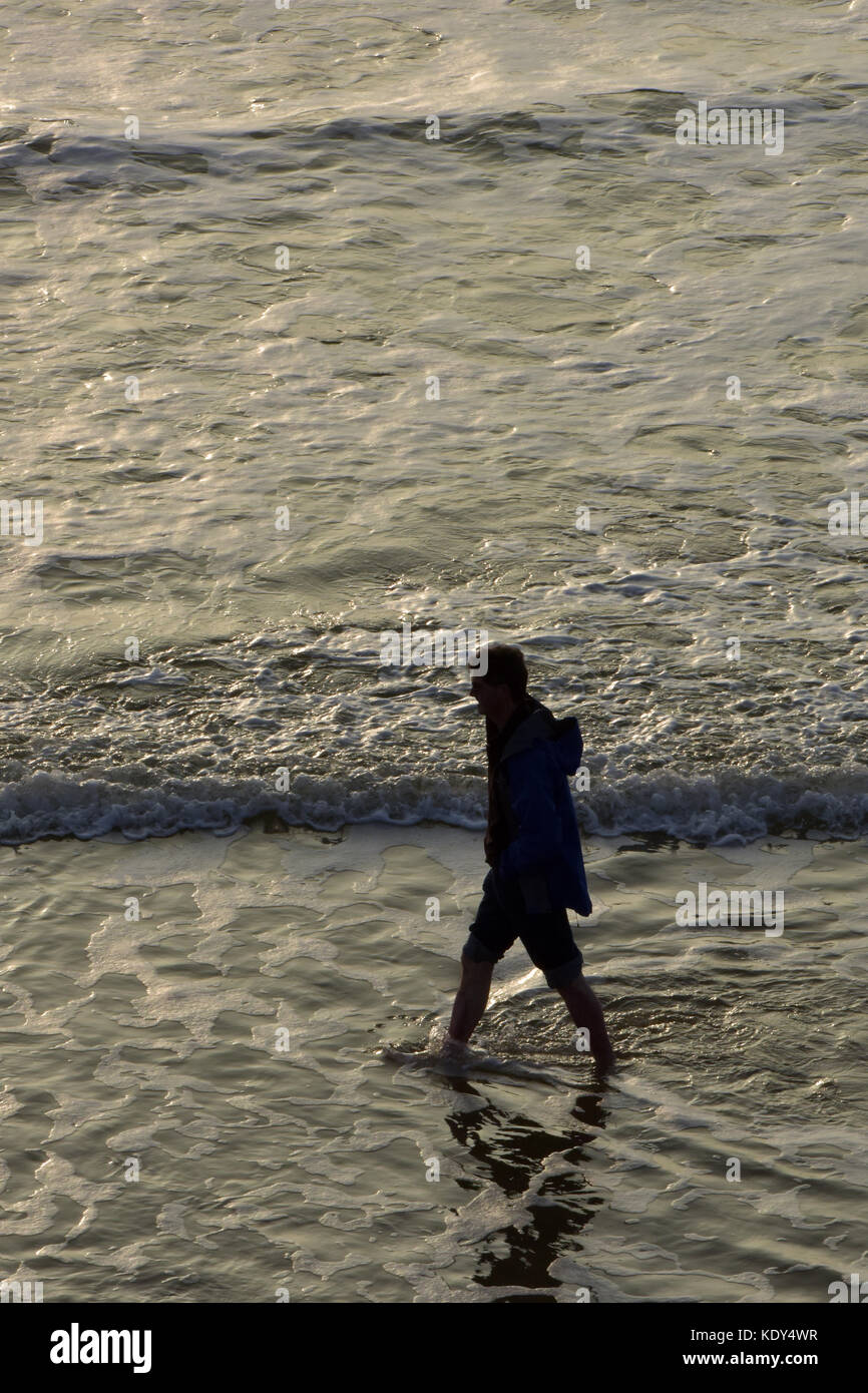 a silhouette of a man walking through the water on the beach at sunset ...