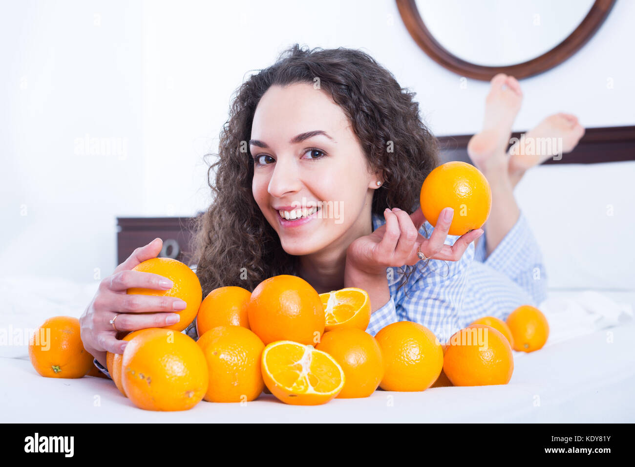 Cheerful female eating oranges in bedroom interior Stock Photo