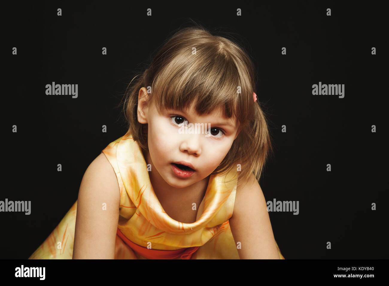 Studio portrait of surprised little Caucasian blond girl in yellow ...