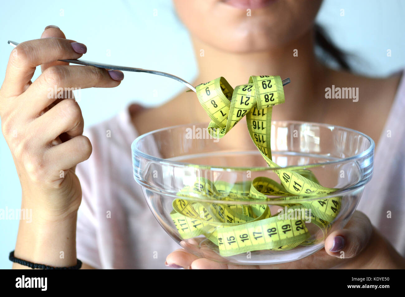 Young woman on diet eating a yellow measurement tape from a transparent bowl, abstract image Stock Photo