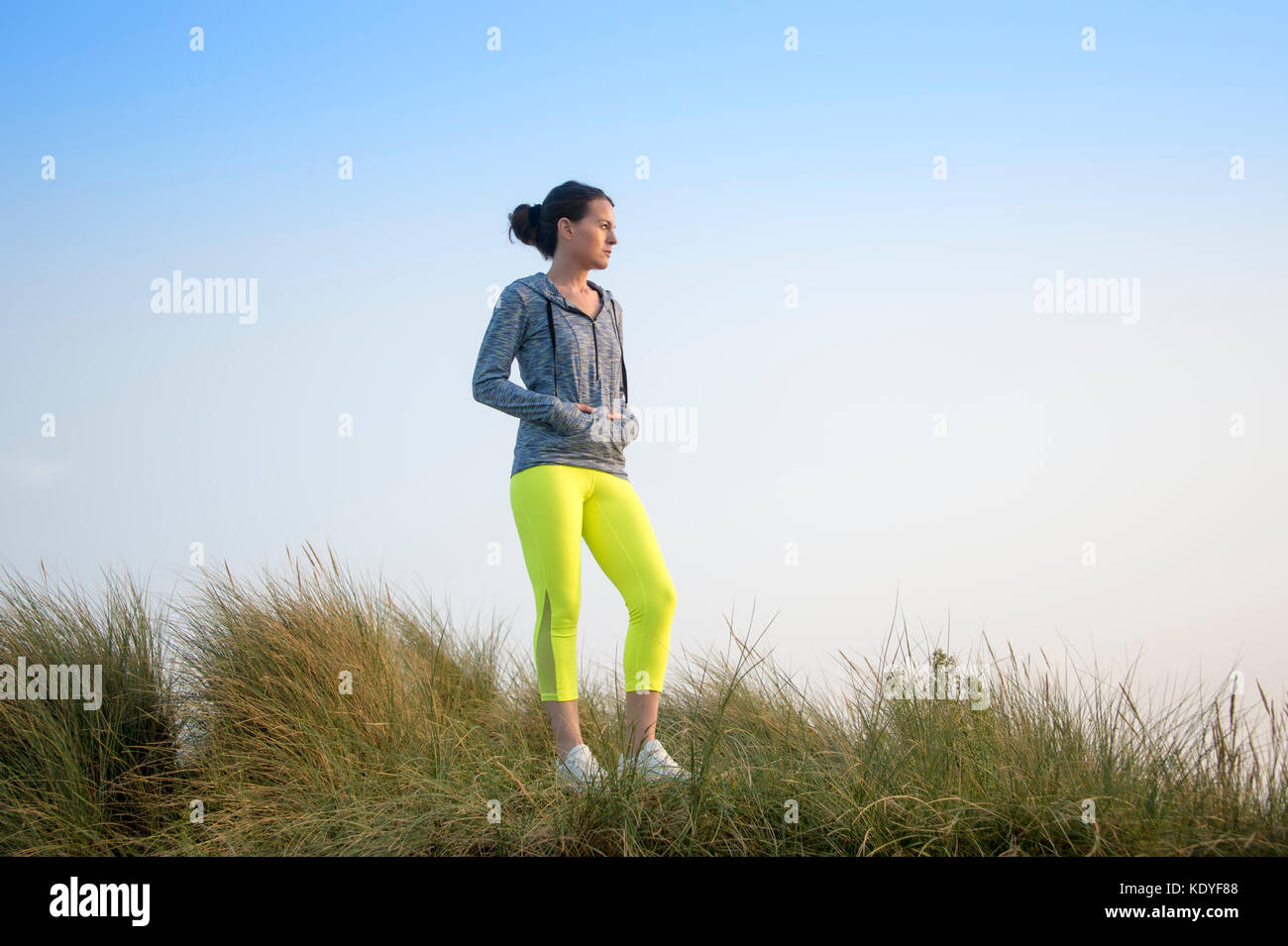 woman standing outdoors wearing fitness wear , resting with hands in hoodie pockets Stock Photo