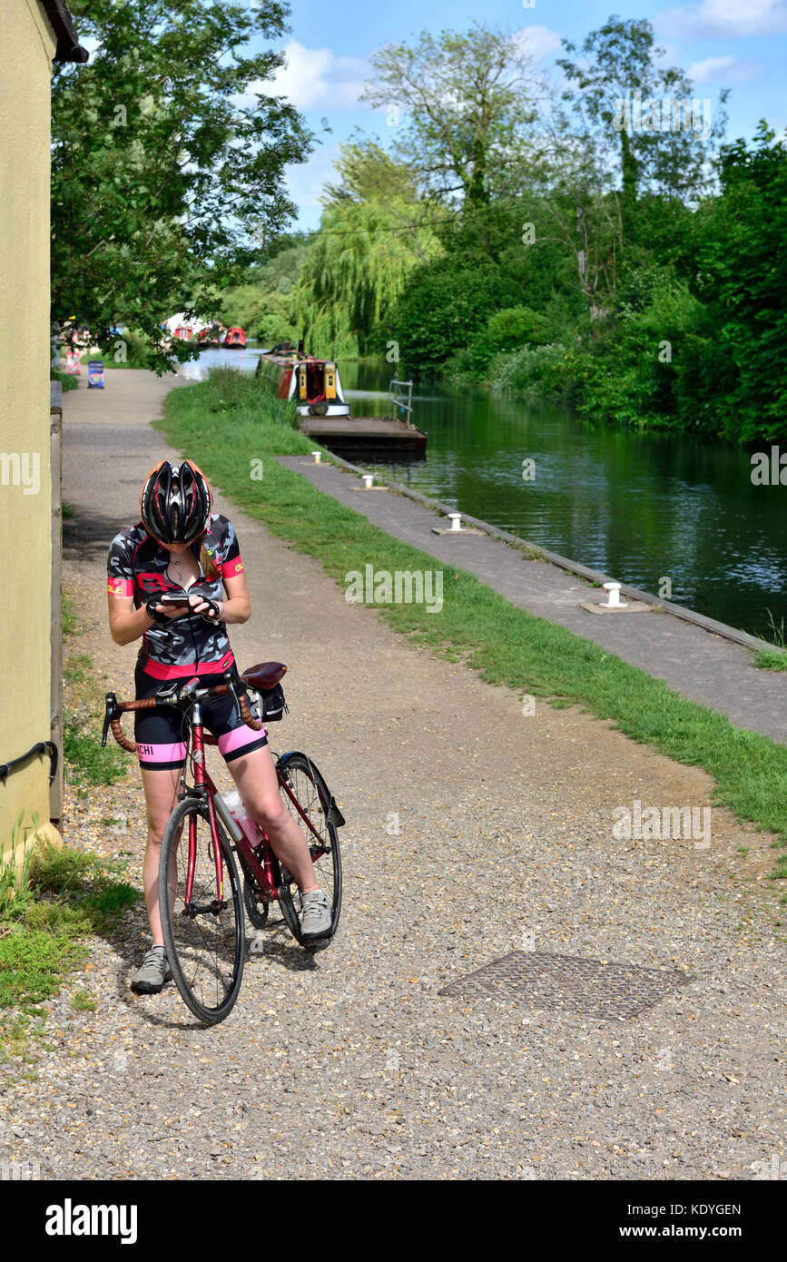 Woman cyclist stopped looking at directions on a mobile phone by canal tow path and cycle way, Theale in West Berkshire, England Stock Photo