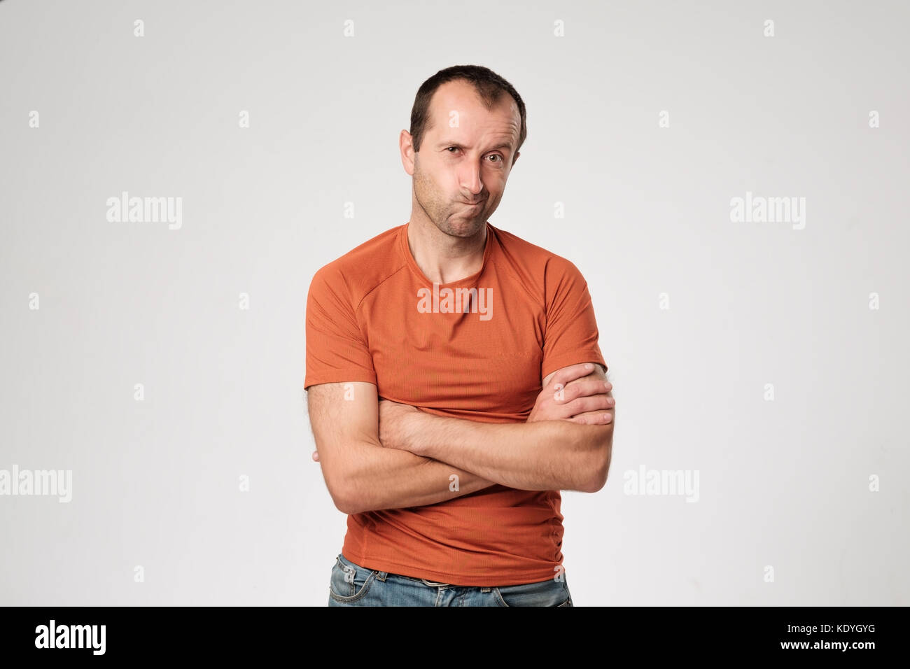 Isolated portrait of angry man wearing orange t-shirt holding arms crossed, having skeptical and dissatisfied look. Stock Photo