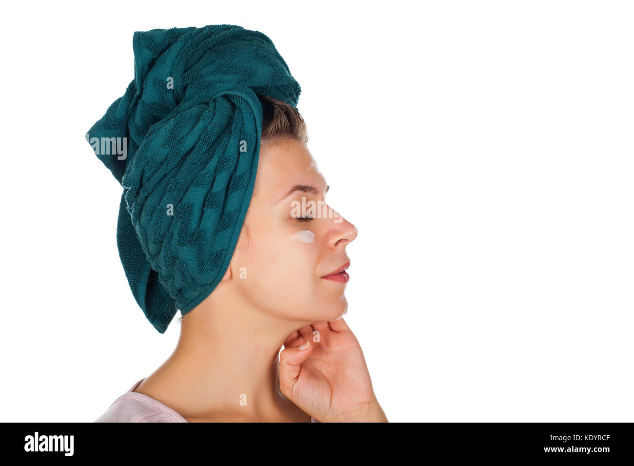 Young woman applying face moisturizer after shower, wearing a towel on