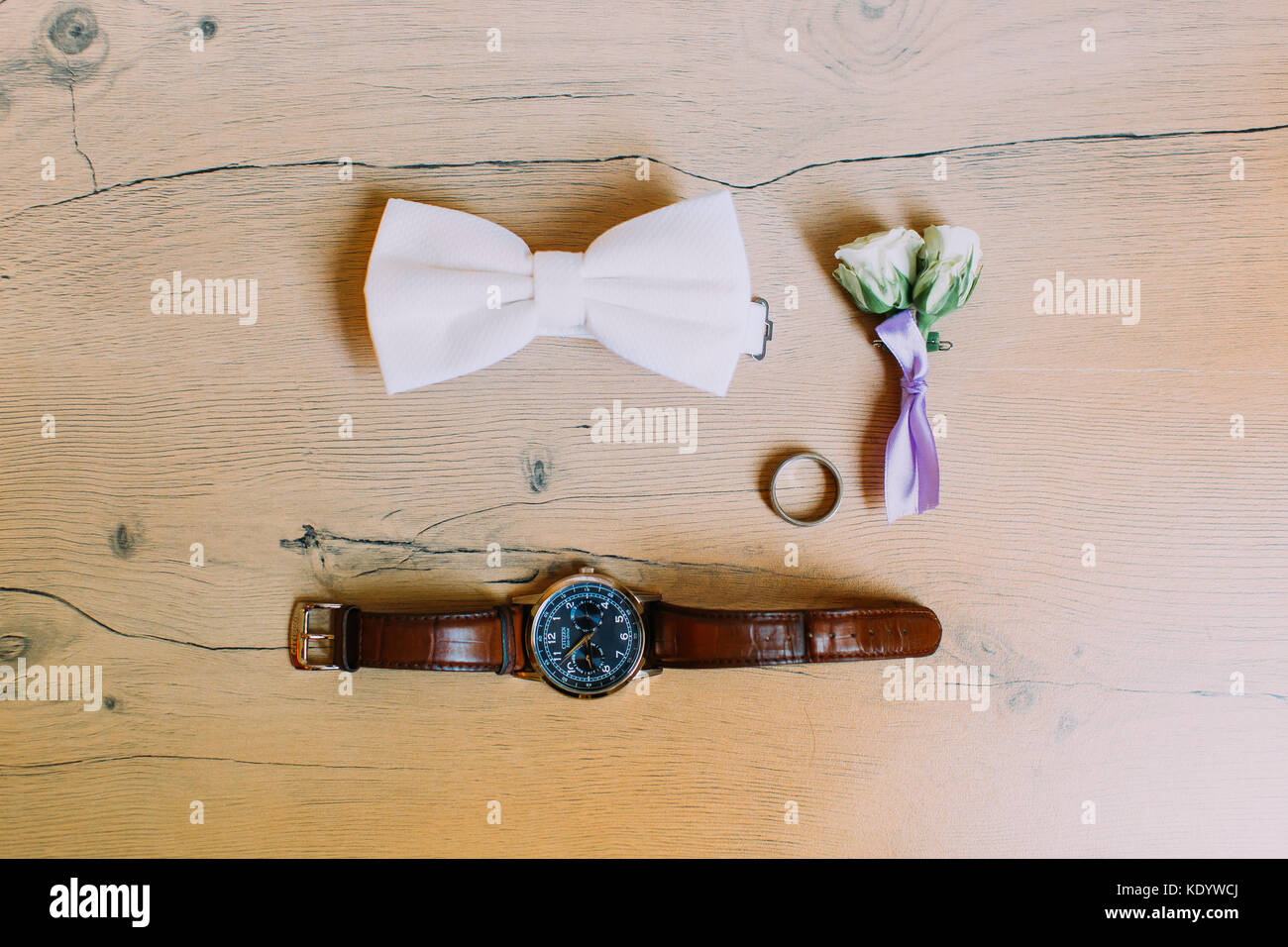 The wedding accessories. The lovely rose boutonniere, hand watch, silver ring and bow-tie on the rustic floor. Stock Photo