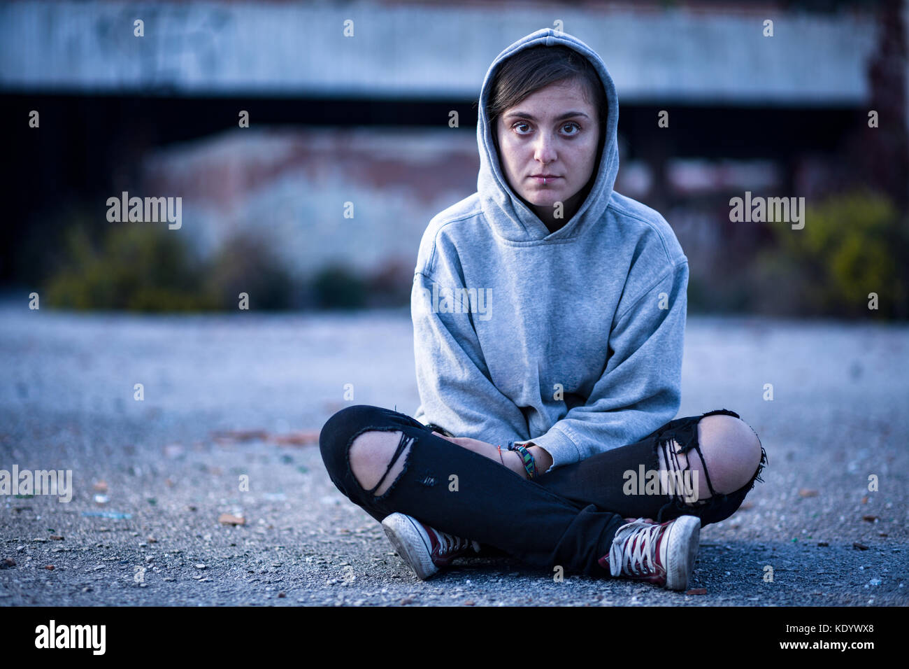 Woman with Sweatshirt and Torn Trousers Sitting on the Street Stock Photo