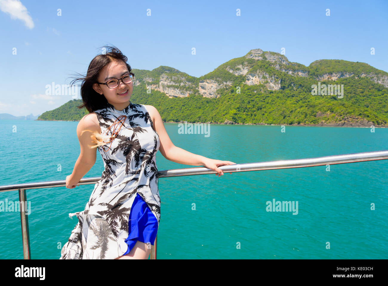 Asian young woman with eyeglasses smiling happily on the boat while cruising the beautiful natural of the blue sea and sky in summer at Mu Ko Ang Thon Stock Photo