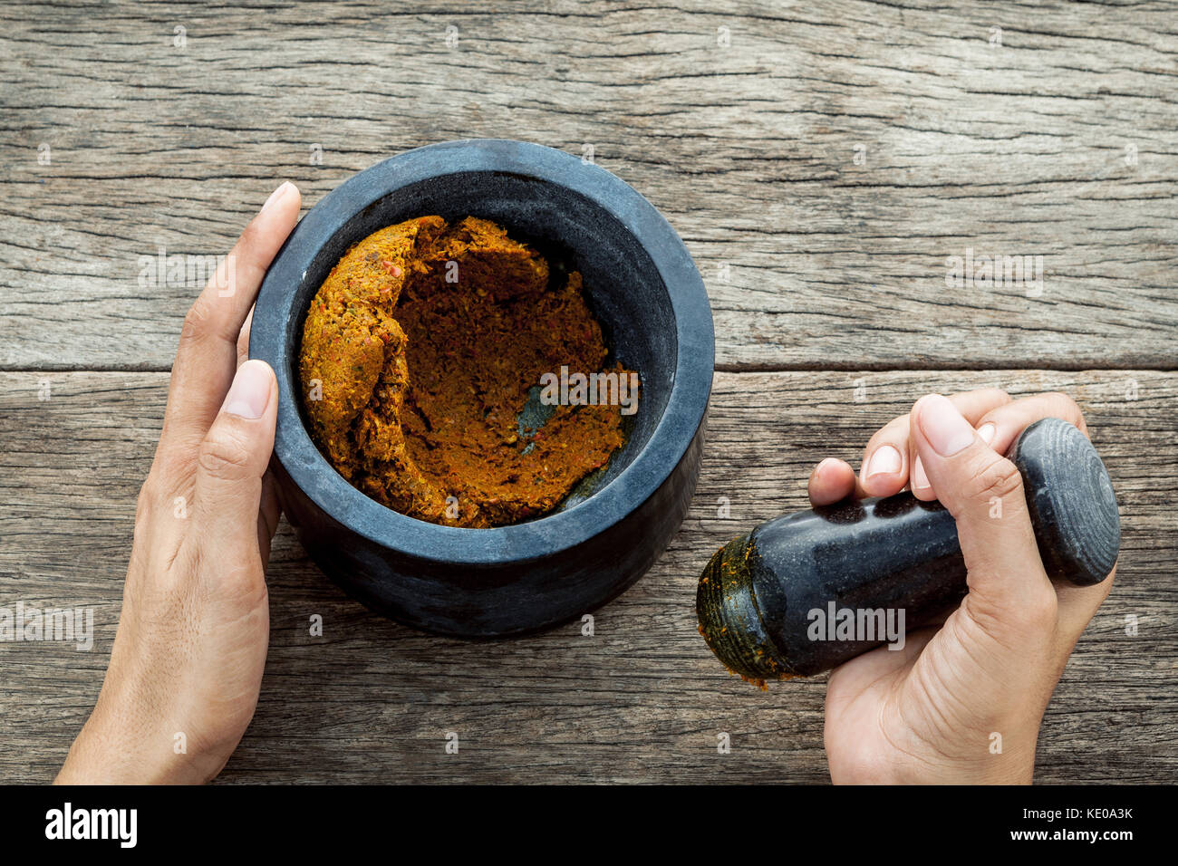 The Women hold pestle with mortar and spice paste of thai popular food red curry  on rustic wooden background. Stock Photo