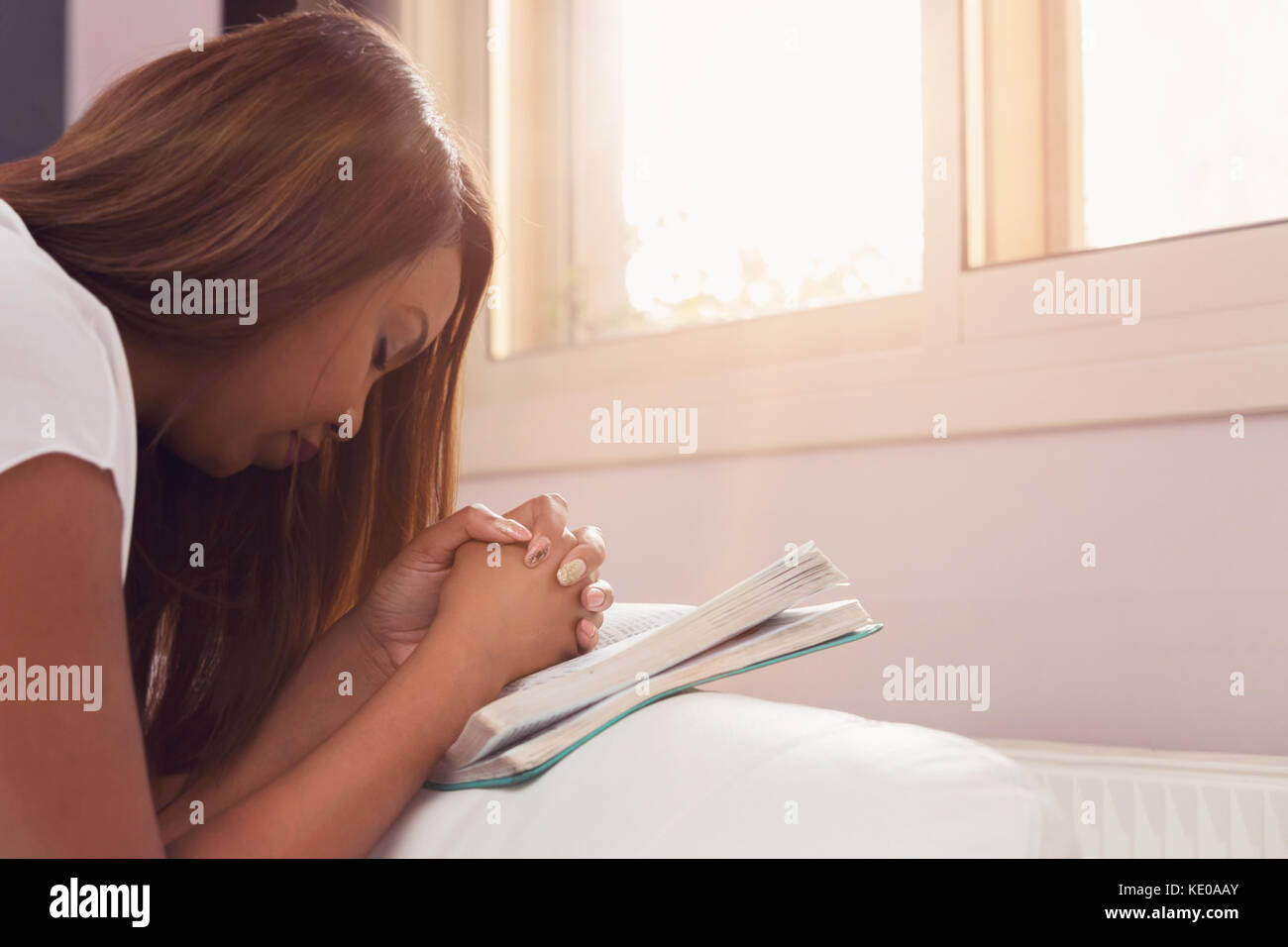 Girl Praying With her Hands Folded On The Bible Stock Photo