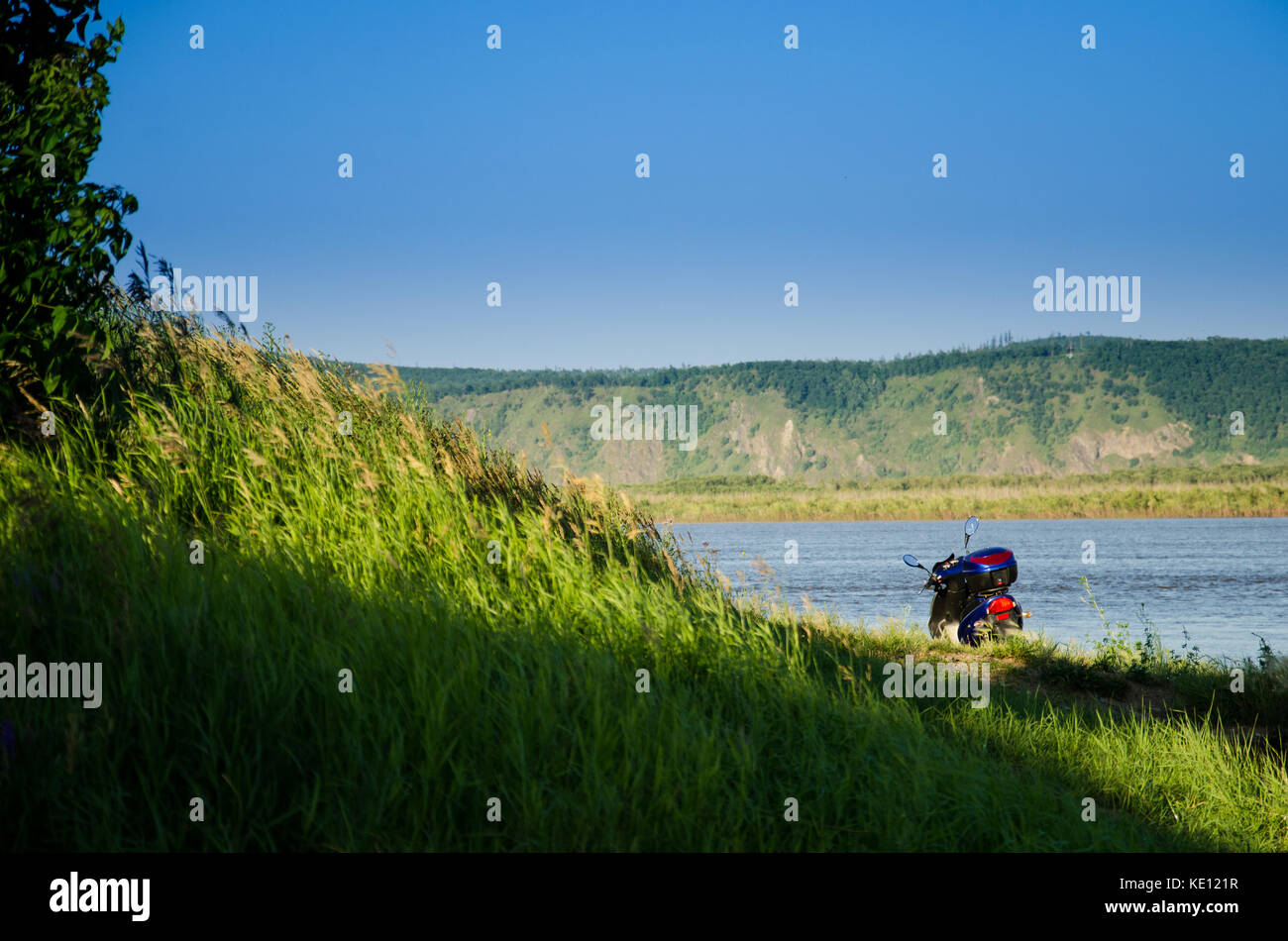 motor scooter near a hill with green grass near the river on a sunny summer day Stock Photo