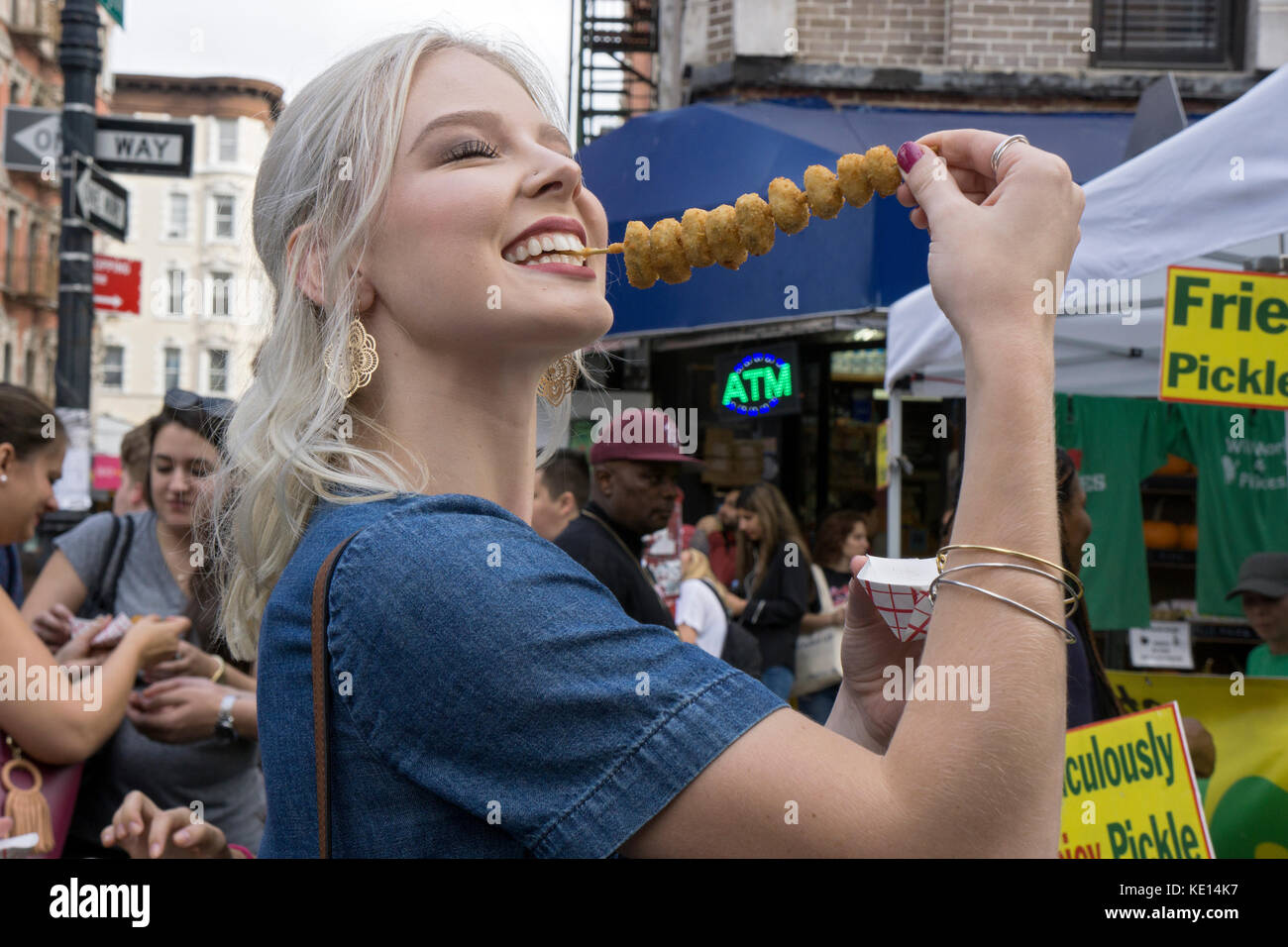 A pretty young lady eating fried pickles at the annual Pickle Day celebration on Orchard Street on the Lower East Side of Manhattan. Stock Photo