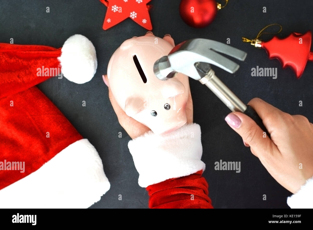 Santa’s helper prepared for high expenses on Christmas time, with piggy bank and hammer on Christmas background Stock Photo