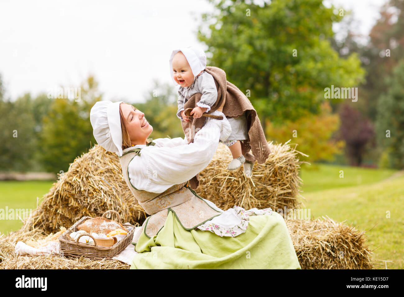 Happy peasant mother with little baby in summer playing on haystack in