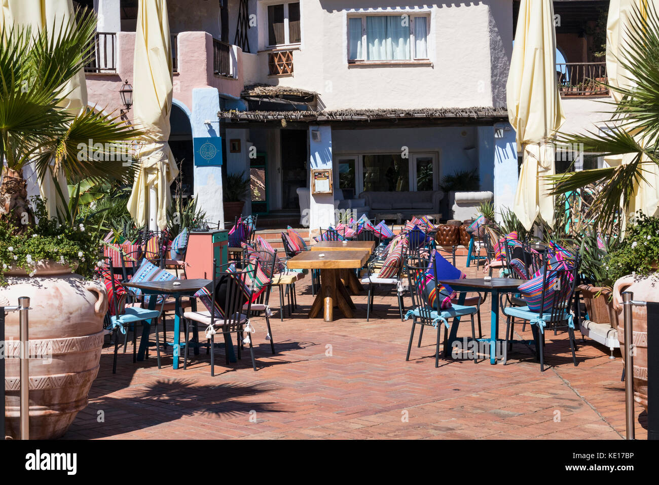 After Lunch: Restaurant Courtyard Seating Area with Colourful Cushions; A Grotto-Style Building. Porto Cervo, Costa Smerelda, Sardinia, Italy. Stock Photo