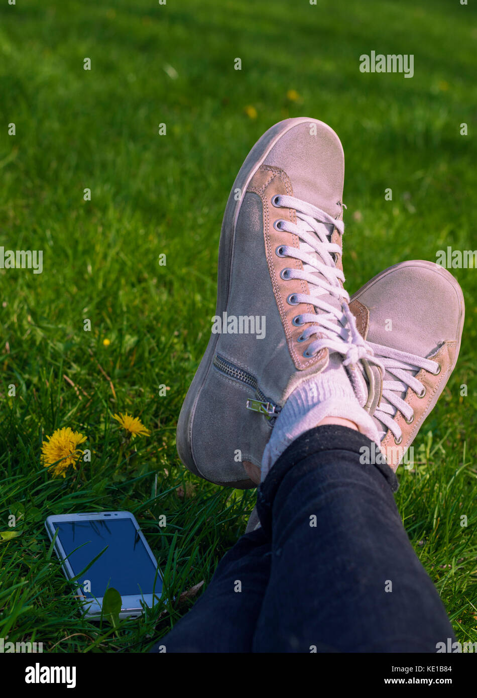 Close up of female lying on grass: snicker shoes and mobile phone nearby  Stock Photo - Alamy