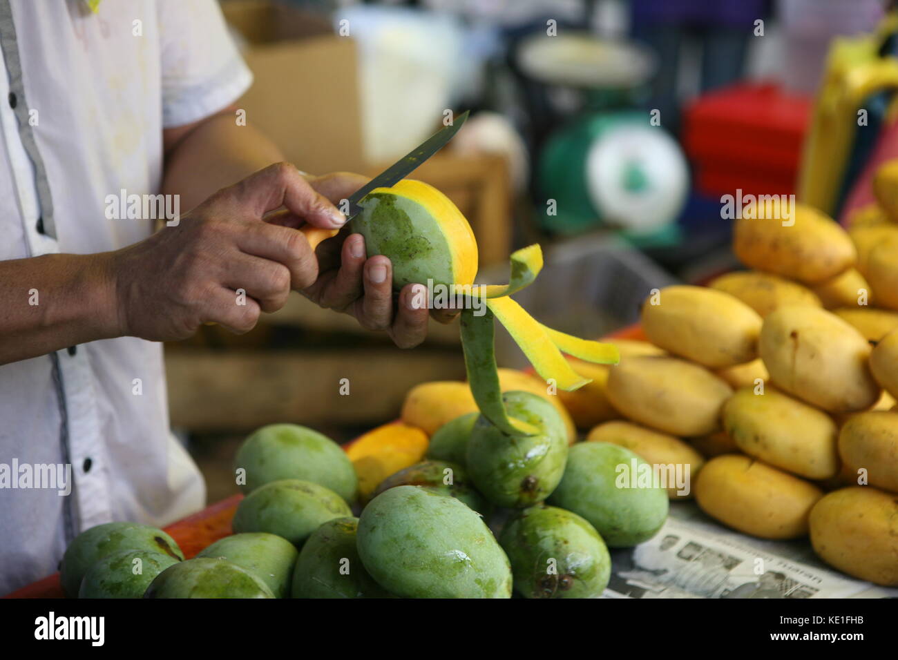 mann der mit Messer eine Mango schält am Marktstand - Man with knife a mango peels at market Stock Photo