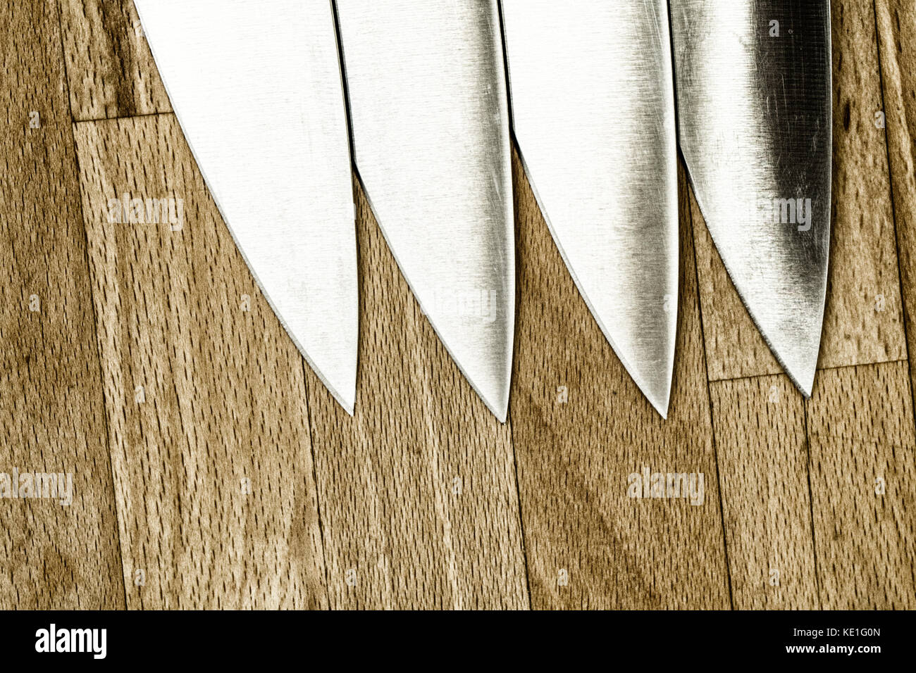 Four identical kitchen knives on a wooden work top Stock Photo