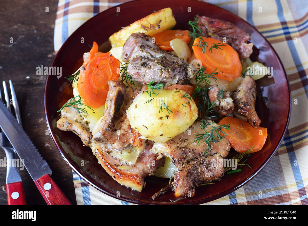 Oven cooked pork with potato, carrots and onion in olive oil and spices in a brown ceramic plate on a wooden background. Home cooking Stock Photo