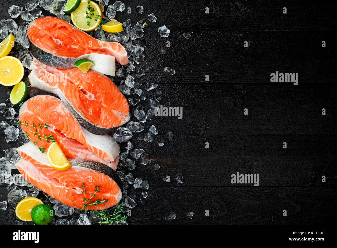Salmon steaks on ice on black wooden table top view. Fish food concept. Copy space Stock Photo