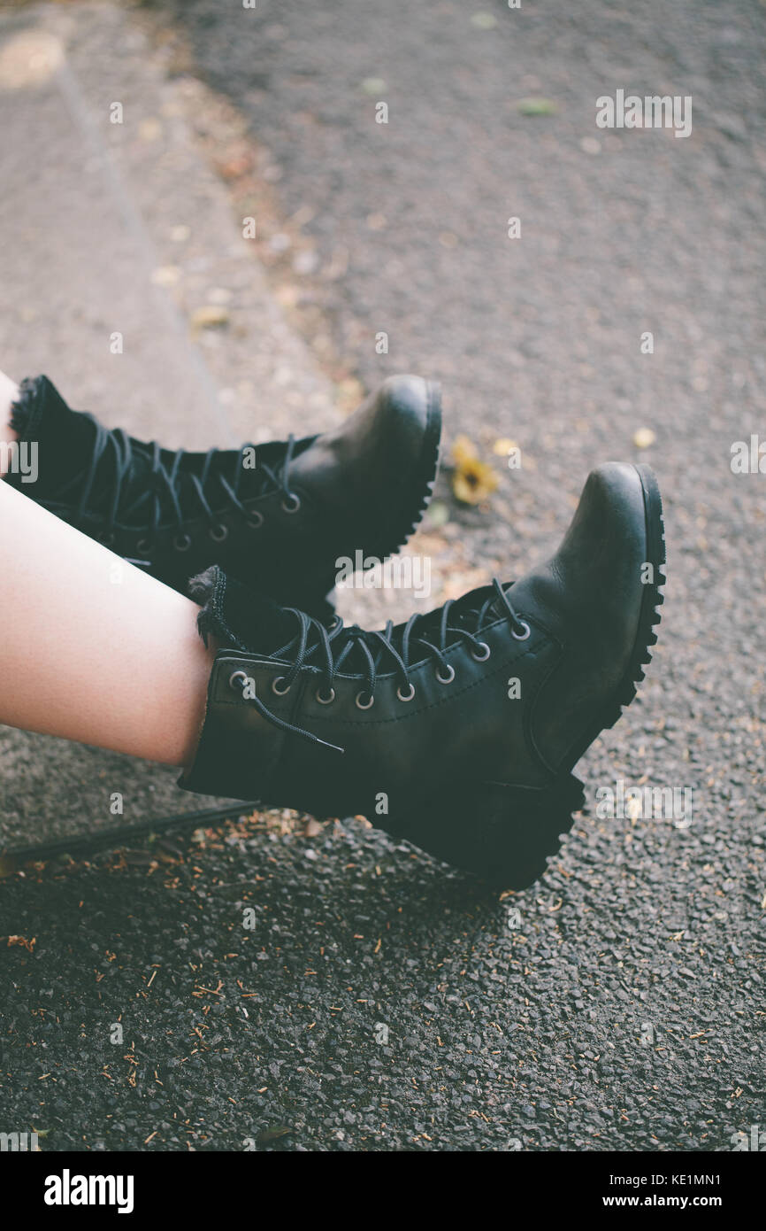 Woman wearing black lace up boots sitting in the street, UK Stock Photo