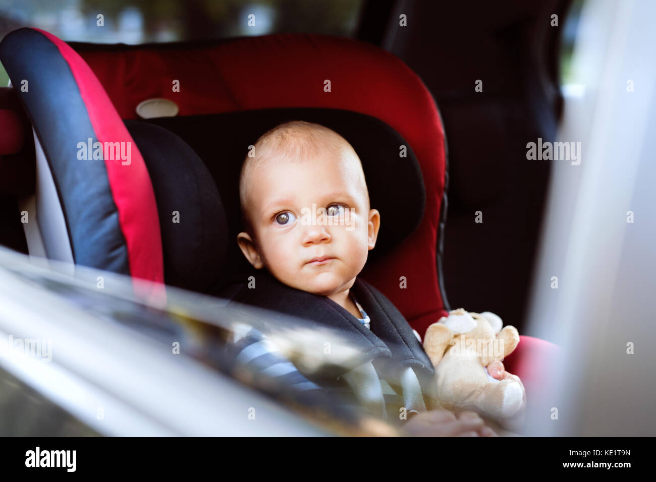 Cute little baby boy sitting in the car seat in the car, looking out. Close up. Stock Photo