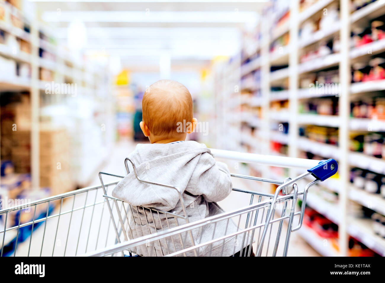 Cute little baby at the supermarket. Baby sitting in the shopping trolley. Rear view Stock Photo