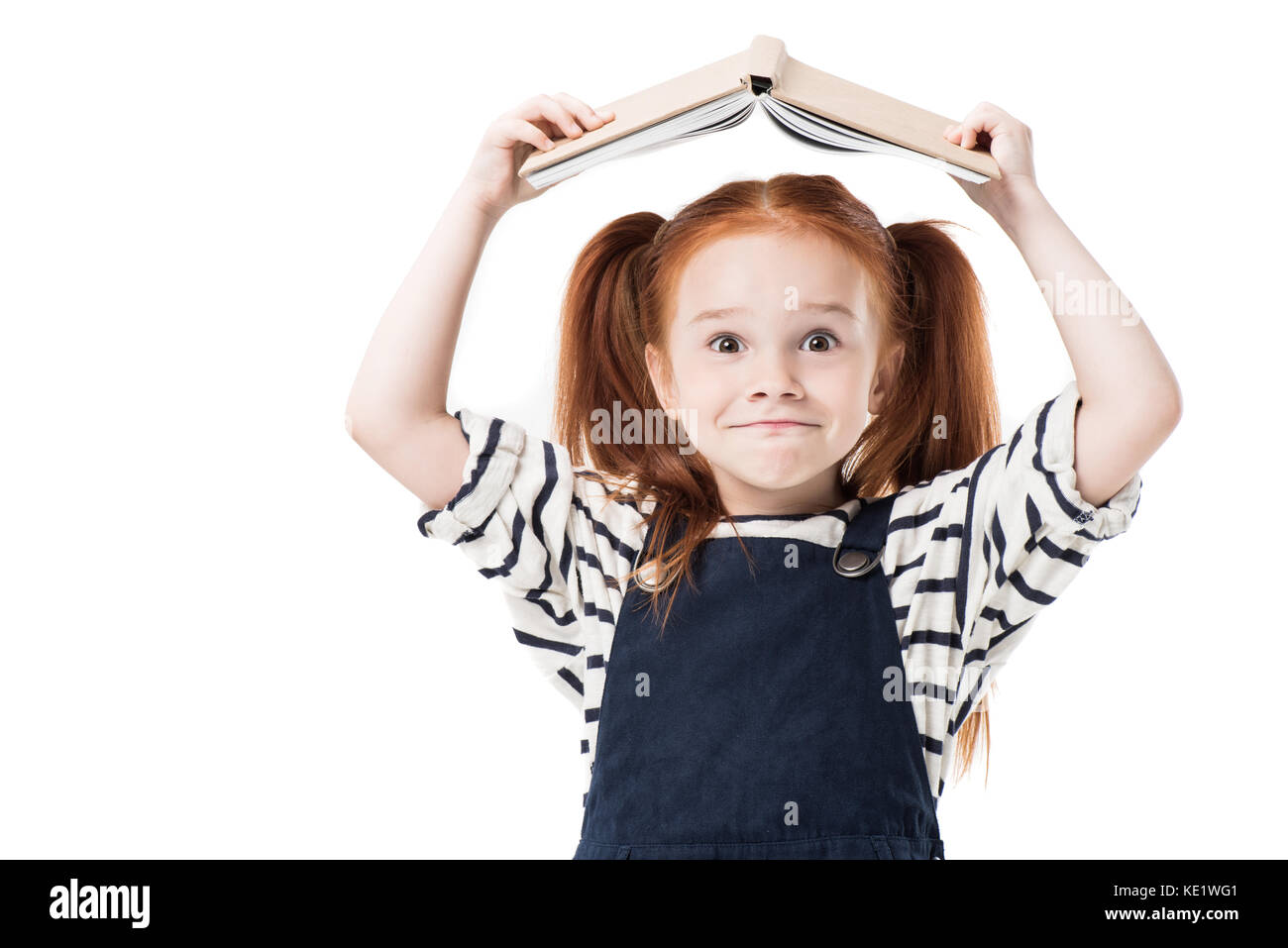 Adorable little schoolgirl holding book and smiling at camera isolated ...