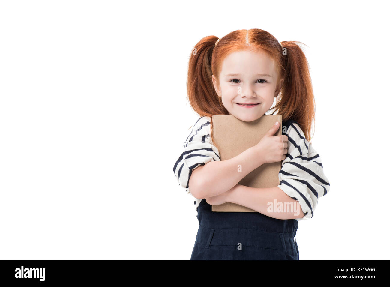 adorable schoolgirl hugging book and smiling at camera isolated on ...