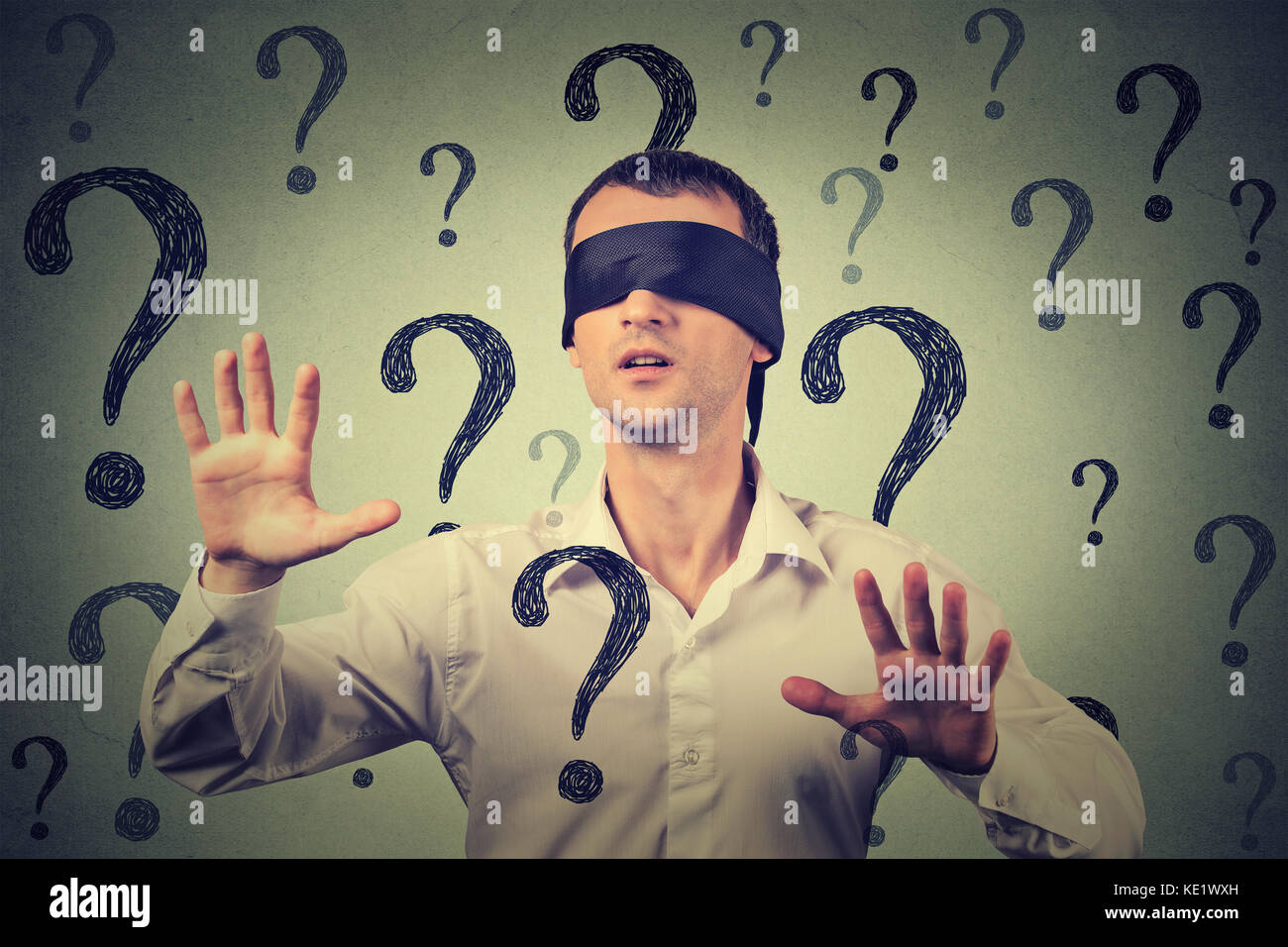 Portrait blindfolded man stretching his arms out walking through many question marks Stock Photo