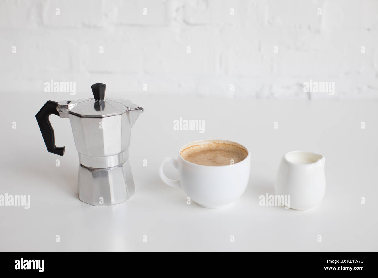 french press, cup of coffee and milk jar standing in row on white table Stock Photo