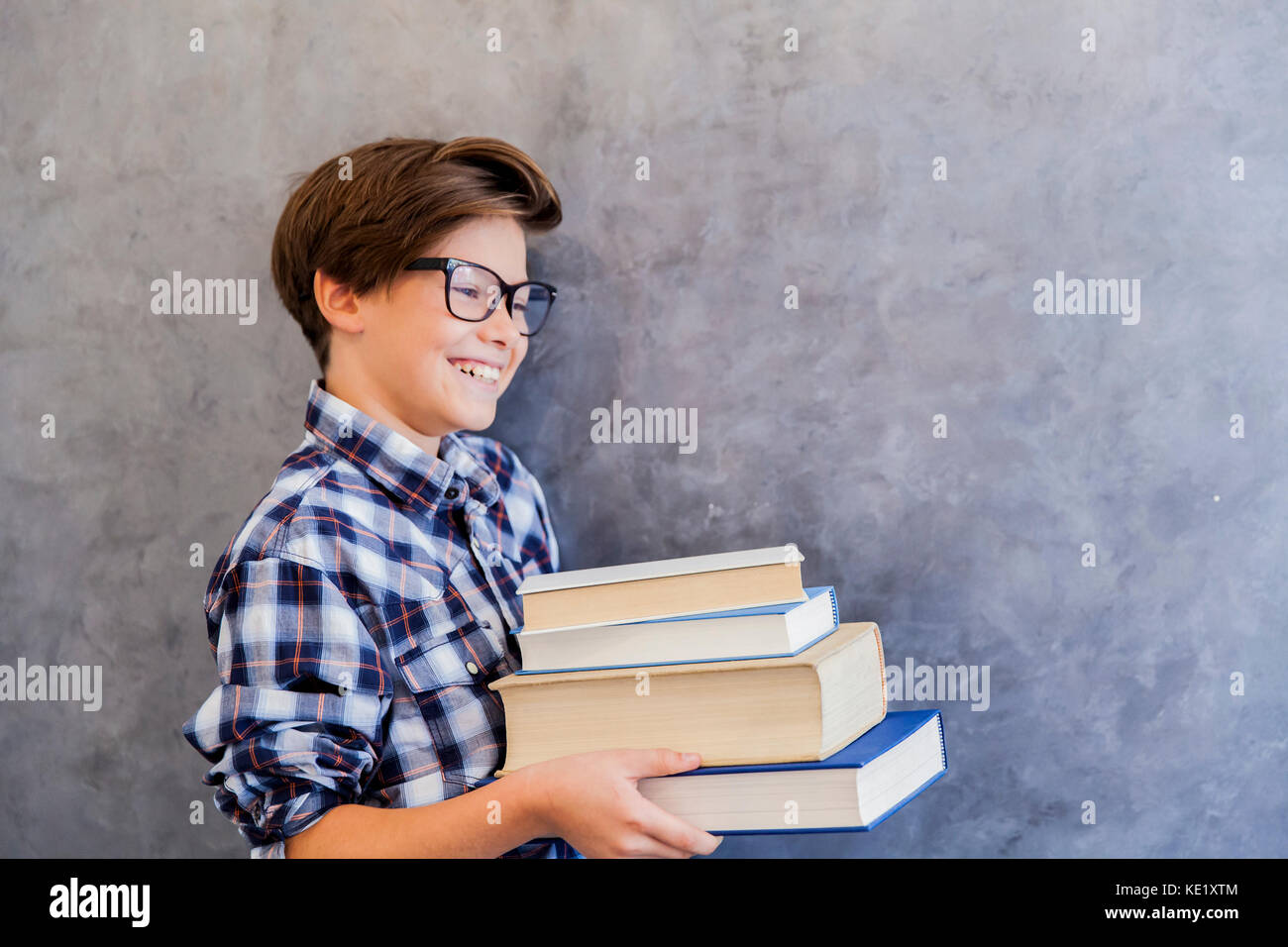 Cute teenage school boy holding books against wall Stock Photo - Alamy