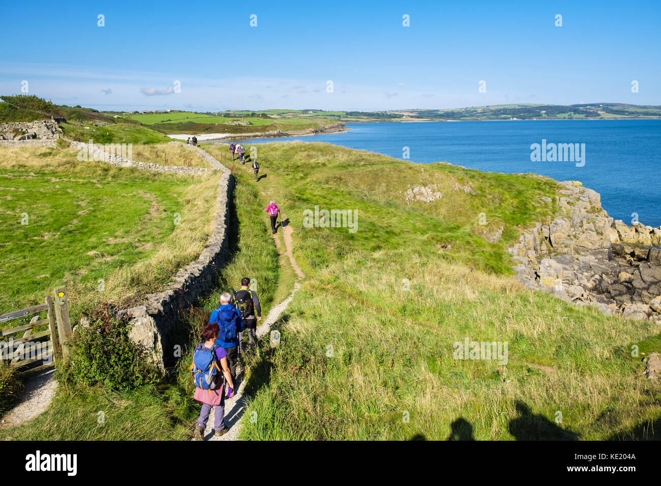 Ramblers on Anglesey Coastal Path walking towards Lligwy Bay from Moelfre, Isle of Anglesey, North Wales, UK, Britain Stock Photo