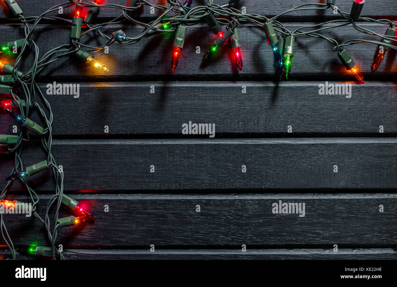 Christmas decoration background, on a black wooden backdrop, with colorful lit christmas lights, framing Stock Photo