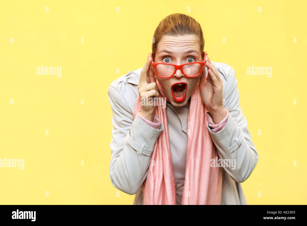 Shocked woman wearing coat, pink scarf, opening mouths , having surprised shocked face. Studio shot Stock Photo