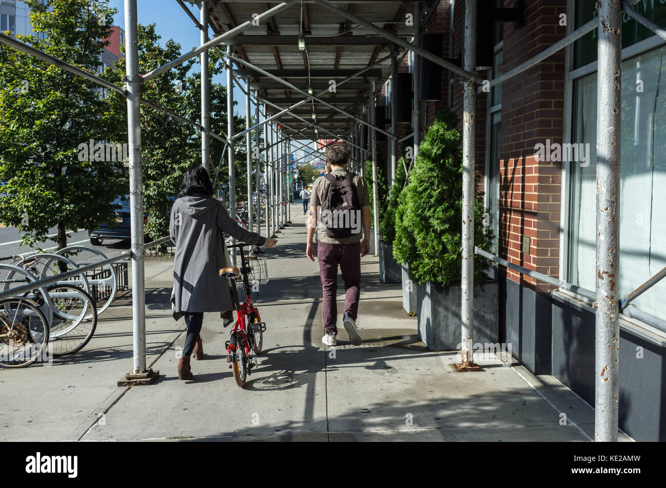 Pedestrians, one with bicycle on Borden Avenue in Queens, New York City. Stock Photo