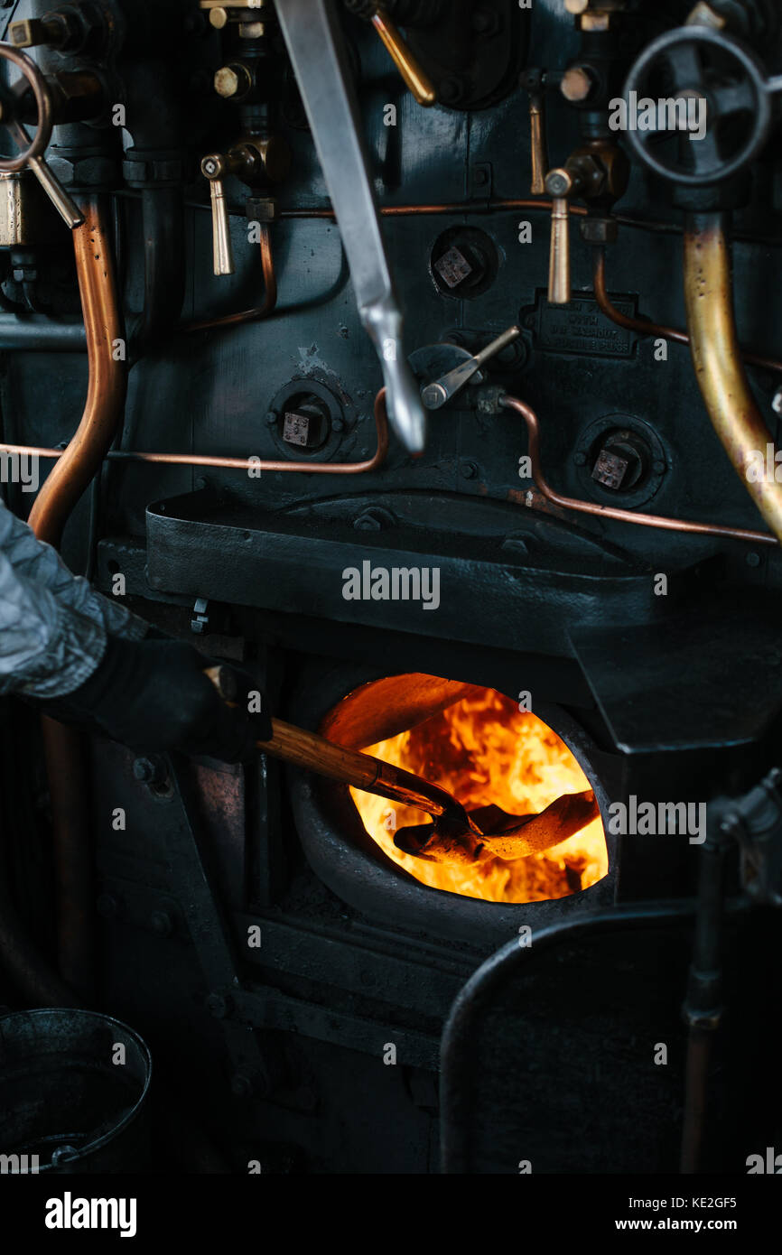 The cab of a steam train with a man shovelling coal into the firebox, UK Stock Photo
