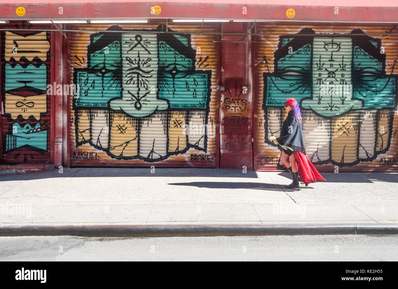 Woman with multi-colored hair walking past closed shutters covered with street art Stock Photo