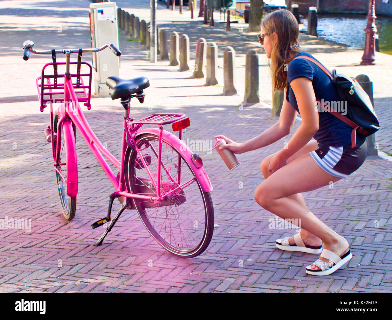 A young woman sprays her bike pink on a street in Amsterdam Stock Photo