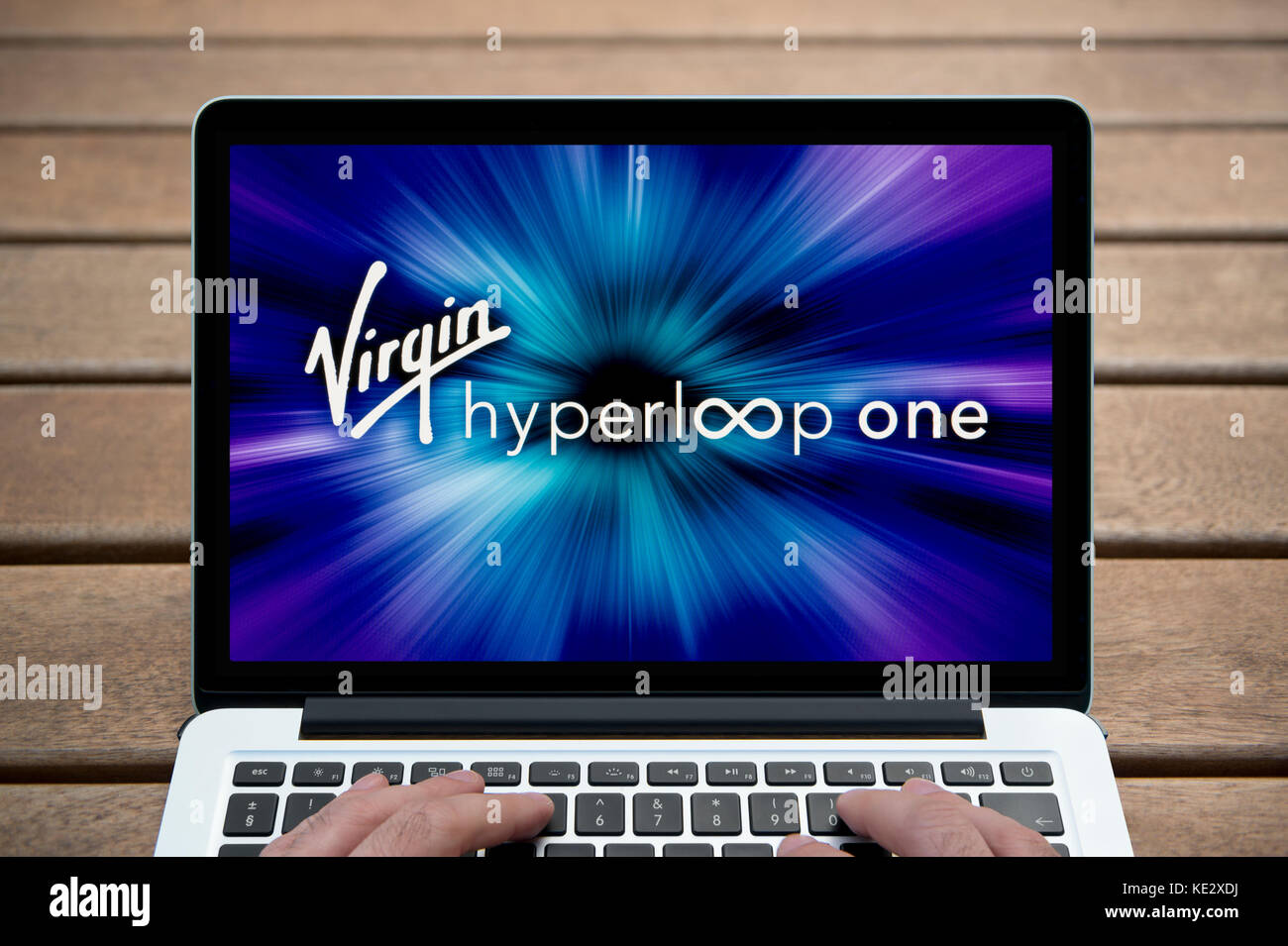 The Virgin Hyperloop One logo is shown on the screen of a MacBook Pro laptop, shot against a wooden bench including a man's fingers (Editorial only). Stock Photo
