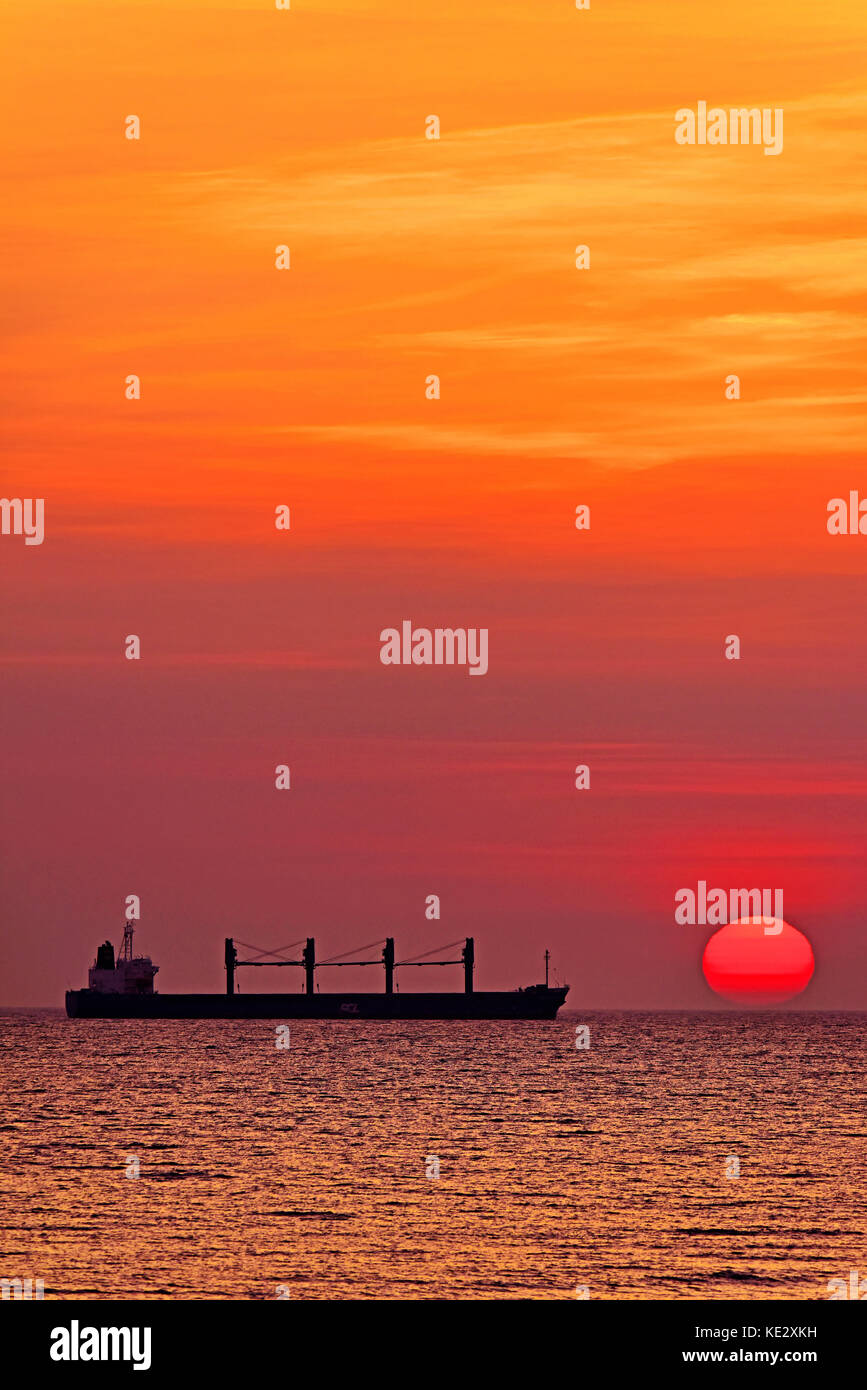 Red sunrise with large sun and PCL Kuok freighter ship in North sea ...