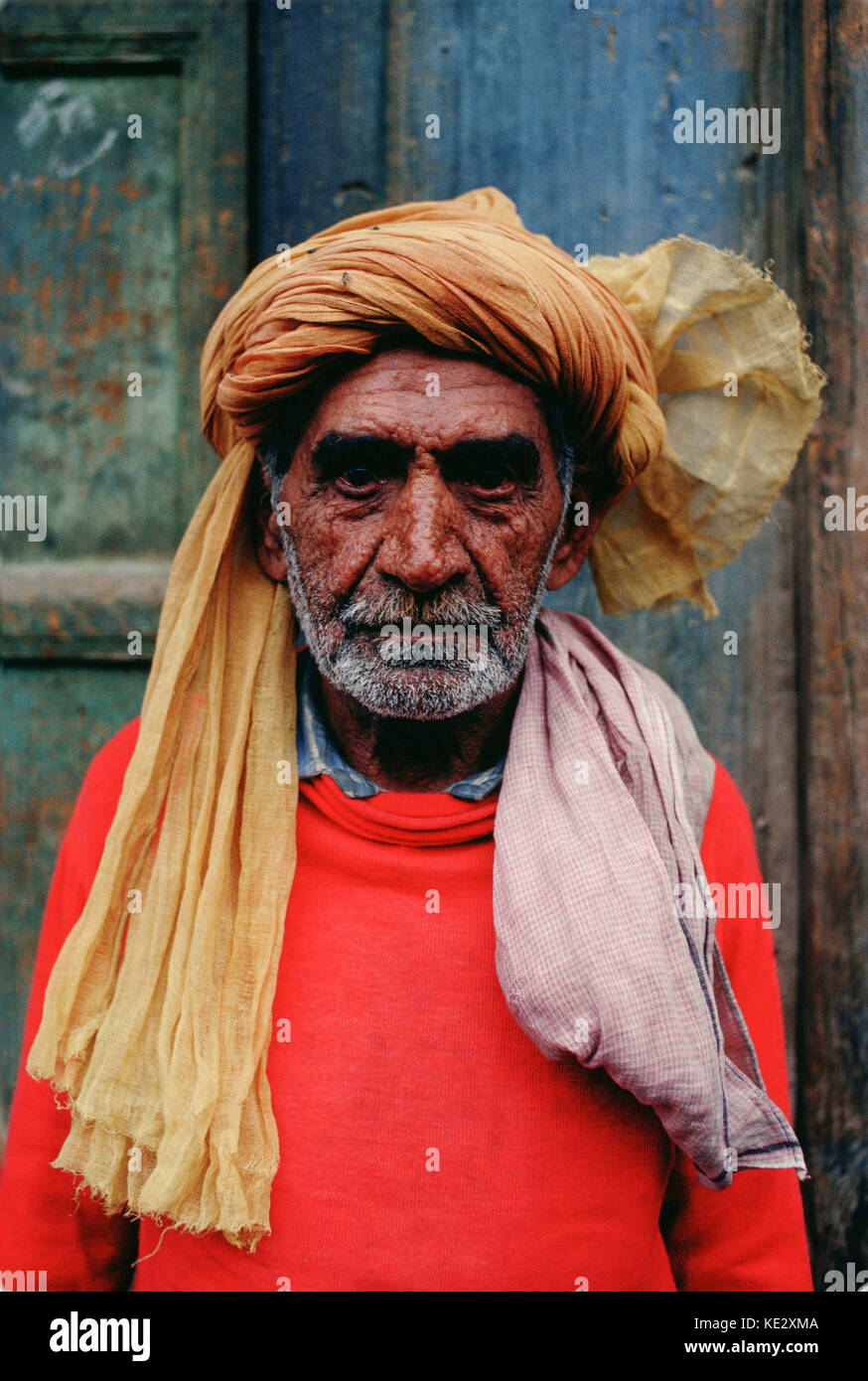 An older man wearing a turban and red sweater stands in front of a ...
