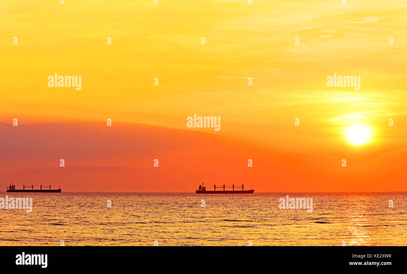 Red sunrise with large sun and PCL Kuok freighter ships in North sea ...