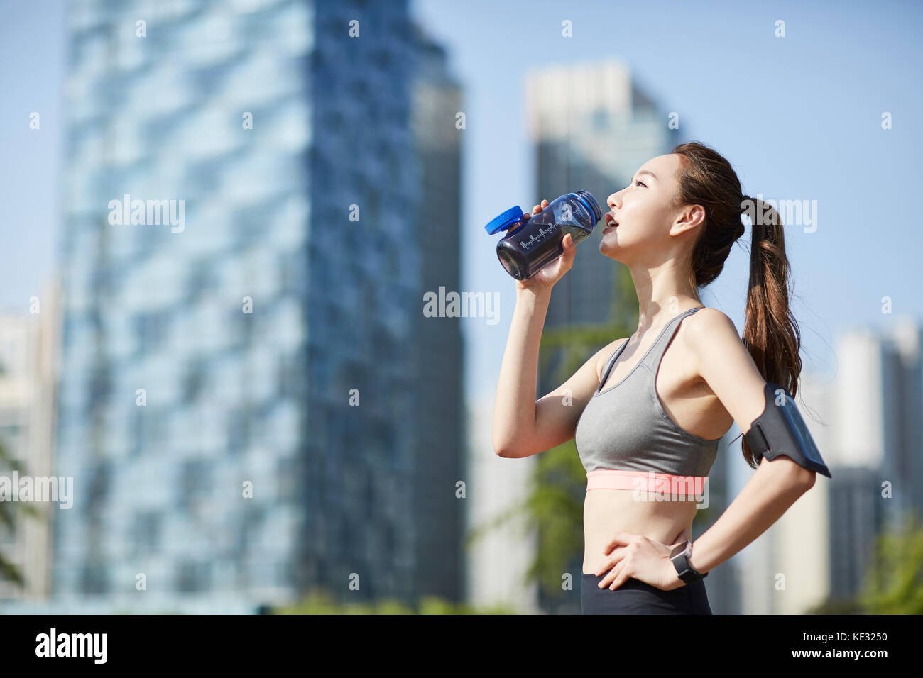 Side view of young slim woman drinking water during exercise Stock
