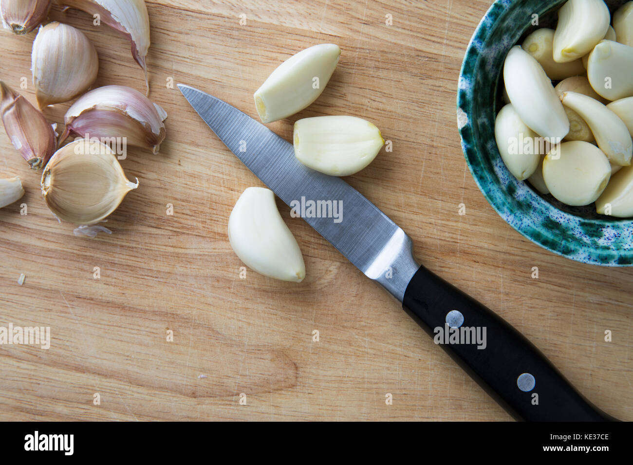 Peeled garlic cloves on cutting board with knife and bowl fro from directly above. Stock Photo
