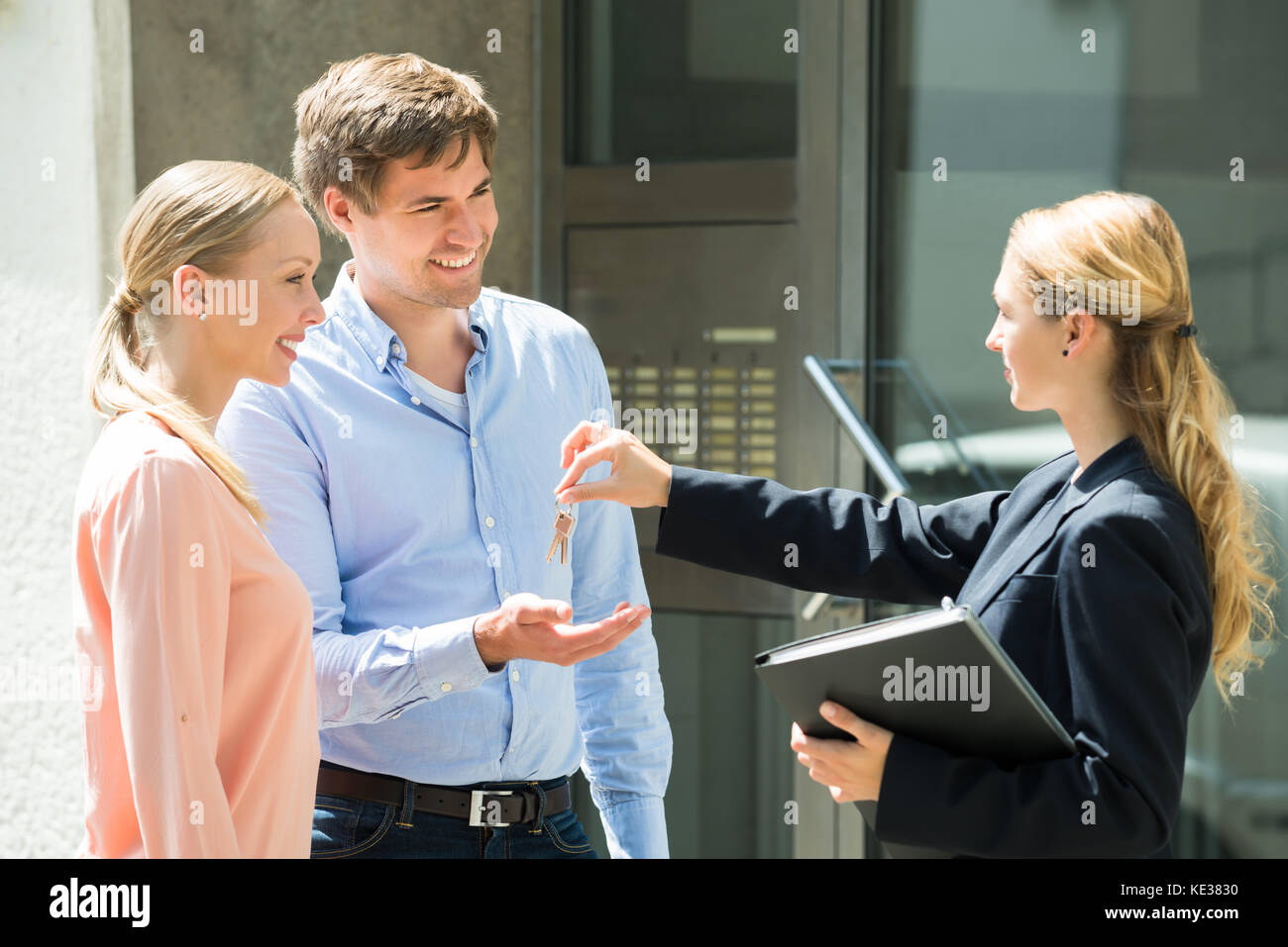 Female Estate Agent Giving House Key To Young Happy Couple Stock Photo ...