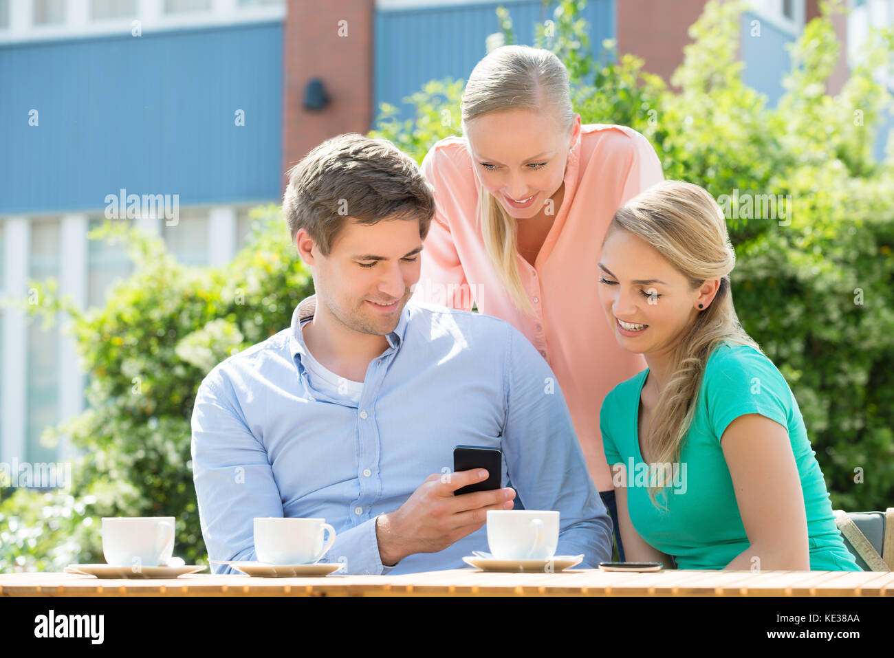 Group Of Happy Young Friends Looking At Mobile Phone In Cafe Stock Photo
