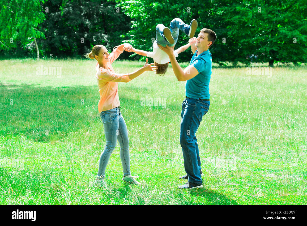 Happy Young Parent Carrying Their Son Upside Down In The Park Stock Photo