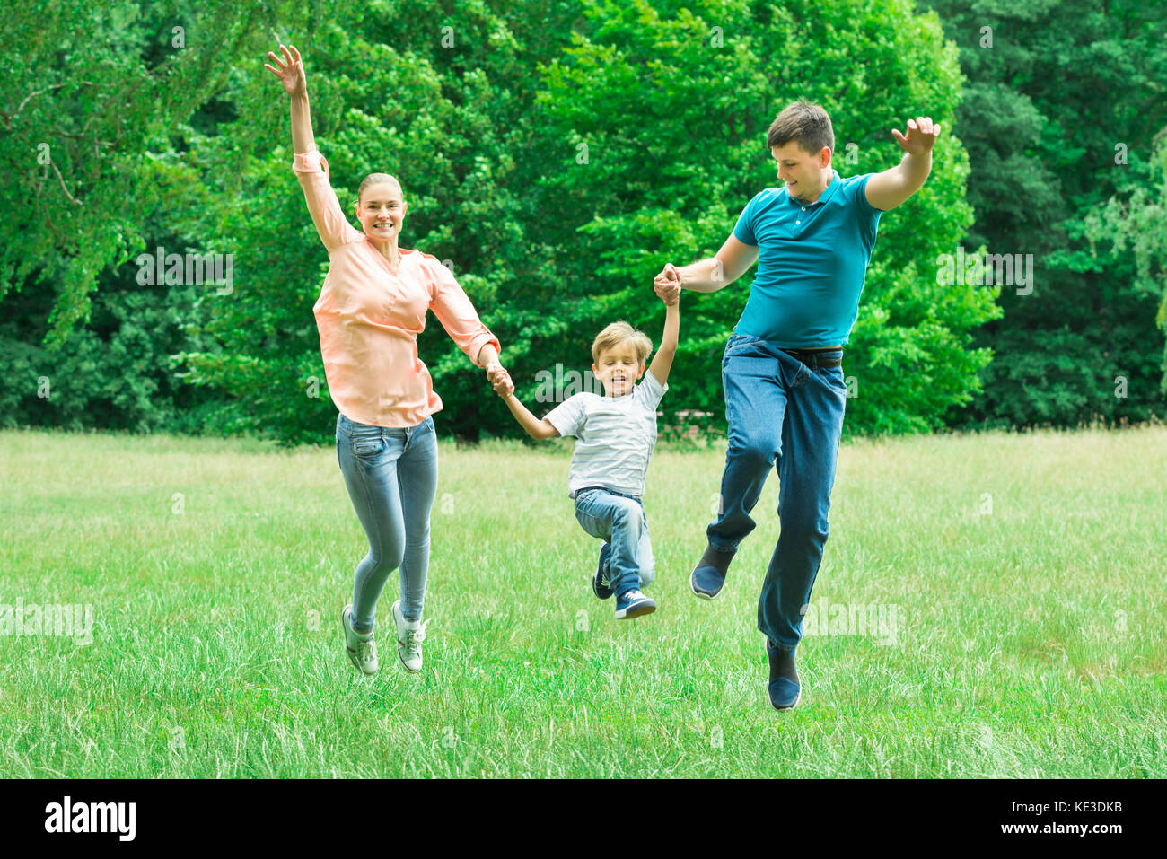 Excited Happy Parents Holding Each Other Hands Jumping With Their Son In The Park Stock Photo