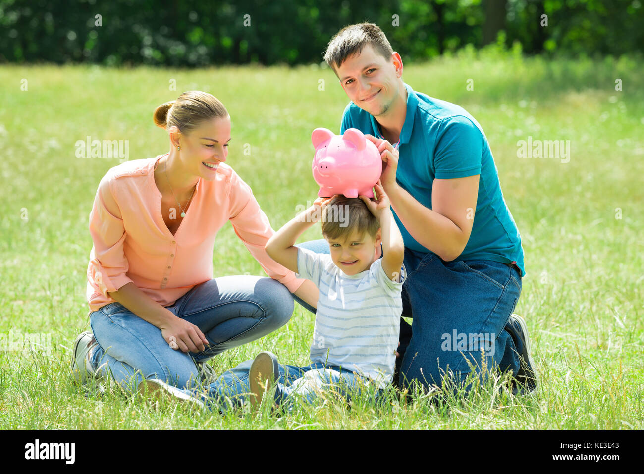 Happy Parents With Their Son Holding Pink Piggy Bank On His Head In The ...