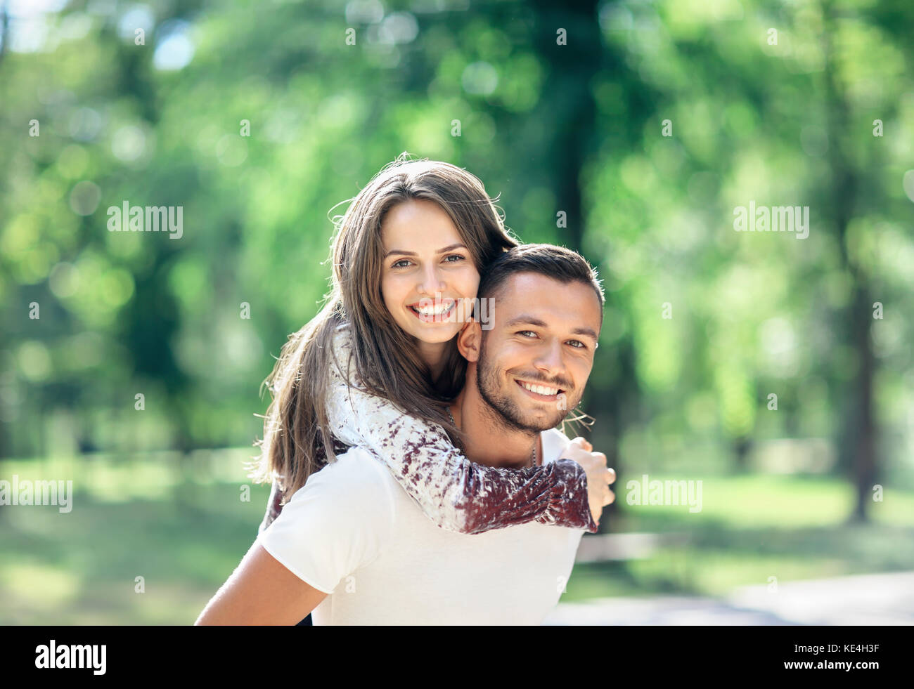 Outdoors portrait of lovers happy young man and woman looking at camera. Smiling girl piggyback of her boyfriend. Love, youth, relationship concept ph Stock Photo
